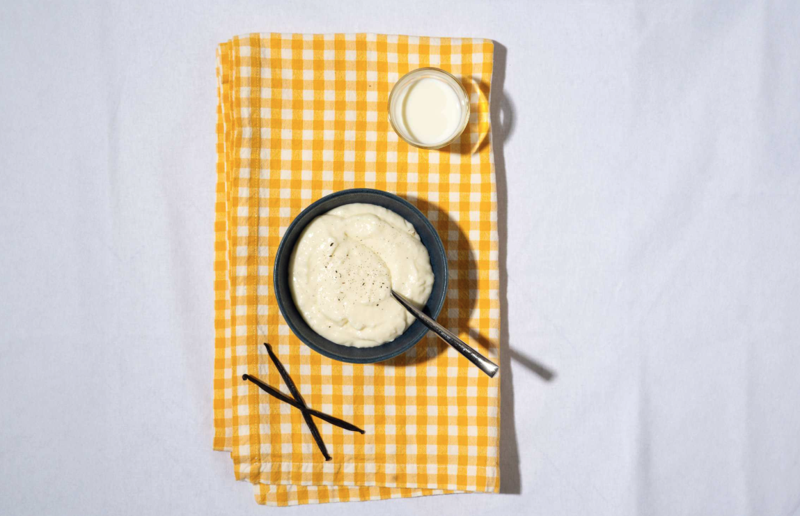 Kulhollinen mango-kookospuuroa keltaruudullisen liinan päällä, vieressä lasillinen maitoa